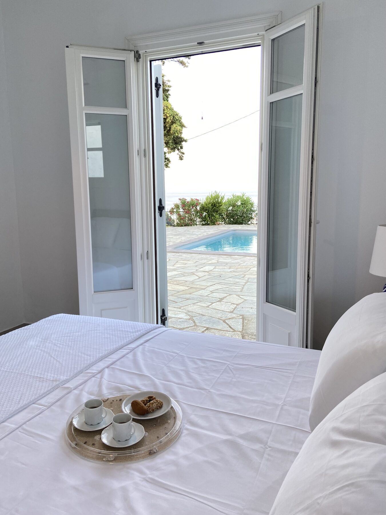 Coffee on a tray in bed, doors open to the pool and the sea