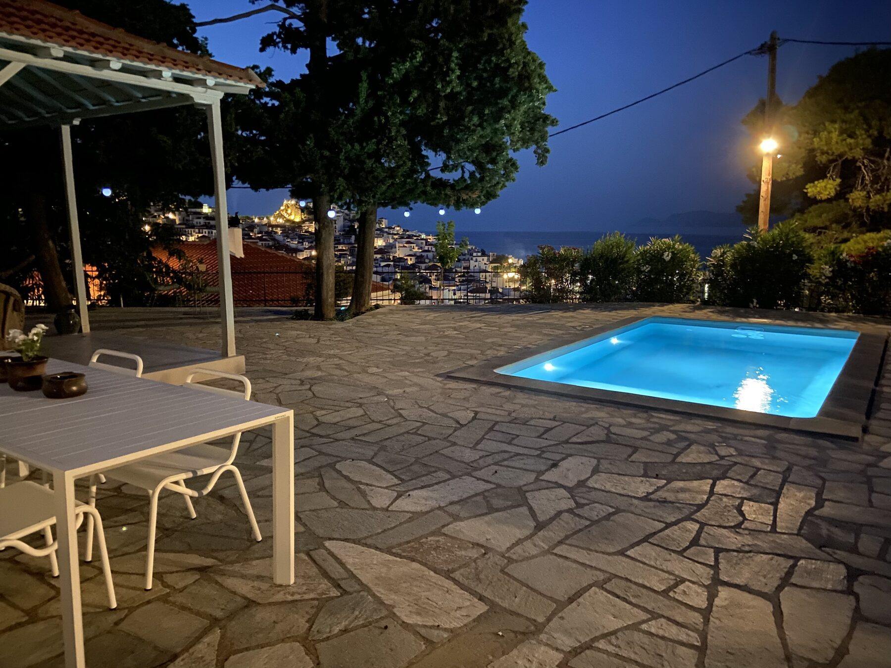 The pool and terrace lit at night above the lights of Skopelos Town
